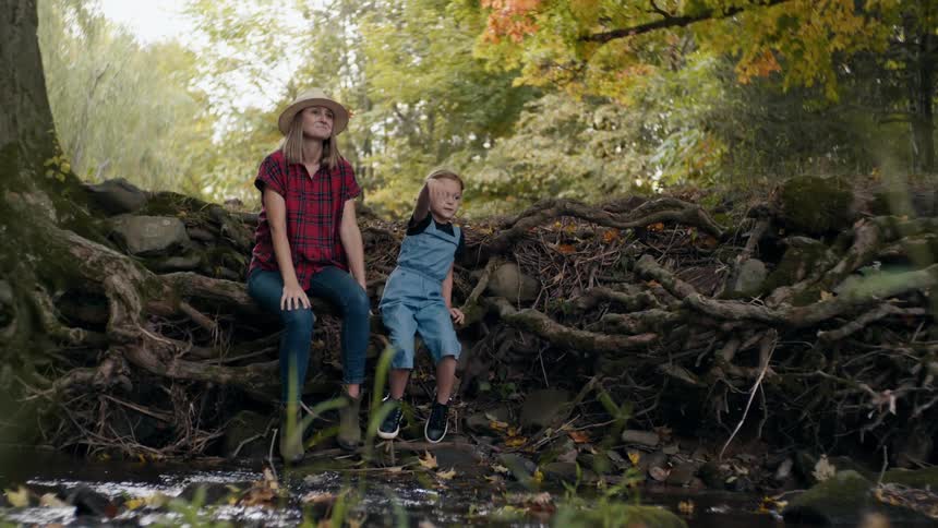 Mother and daughter sitting on a tree trunk in a forest while the daughter throws a rock