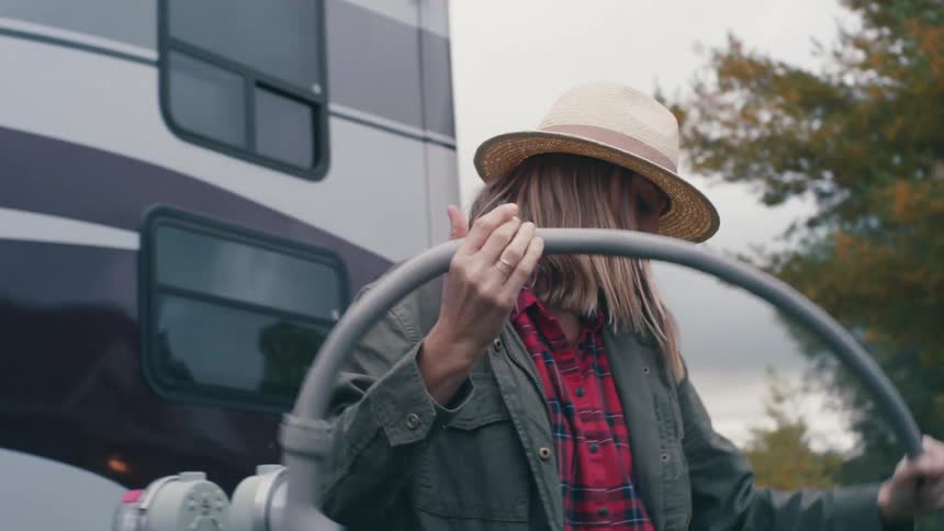 Woman pulling a tube attachment towards an rv outside at daytime