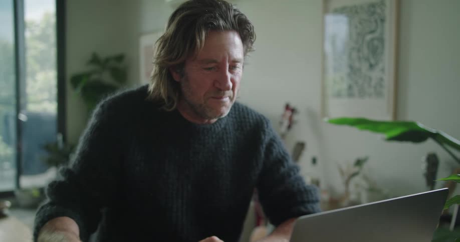 Man video chatting on a laptop computer in a living room drinking from a mug