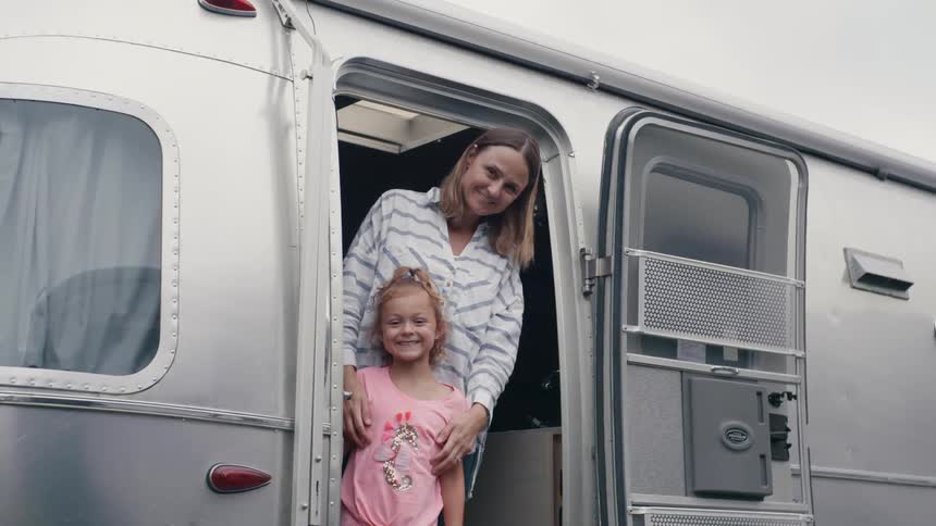 Mother and daughter smiling at the camera from the door of a caravan