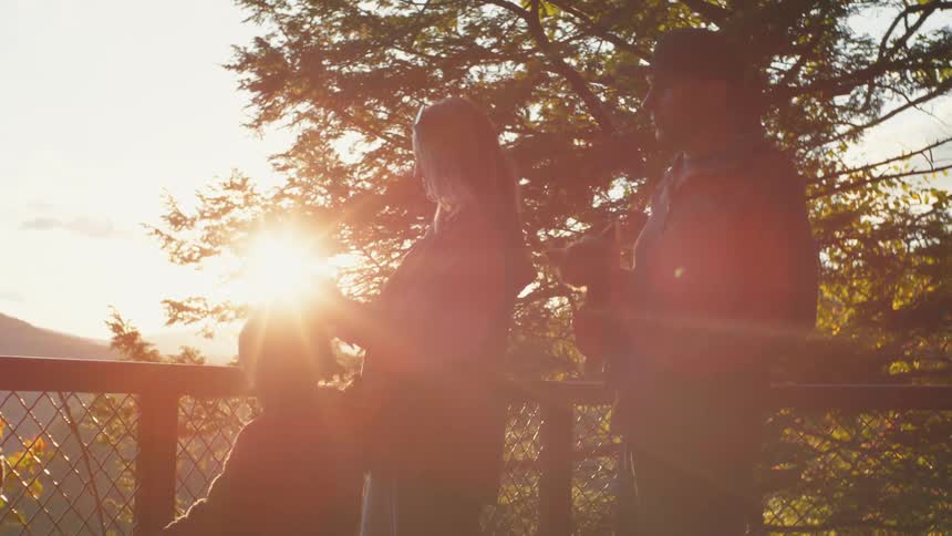 Mother standing next to her husband and daughter outside next to a metal fence at sunset
