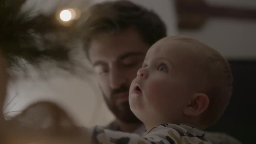 A man is holding a child as he looks up at a christmas tree
