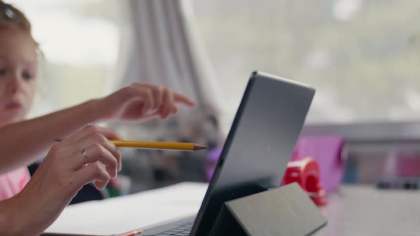 Mother and daughter pointing at the screen of a tablet while doing homework