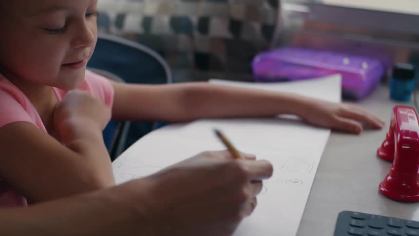 Little girl sitting at a desk at home with school work in front of her writing with a pencil and studying