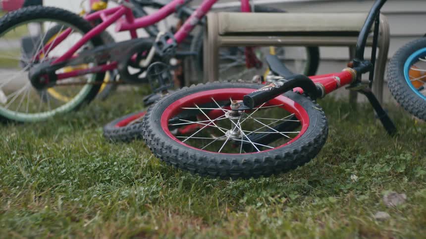 A red bike lays on grass next to other bikes with the front tire spinning