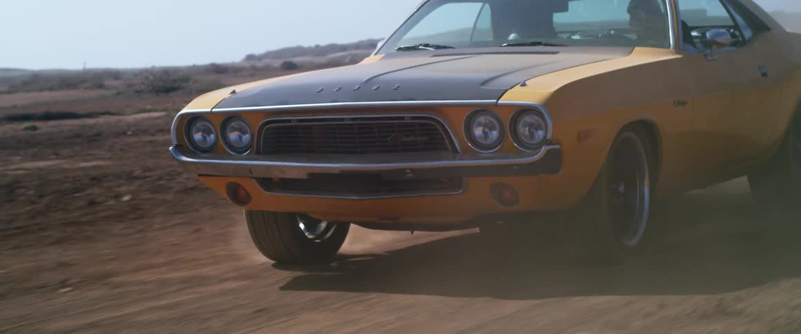 A black and orange car drives down a dirt road on a sunny day