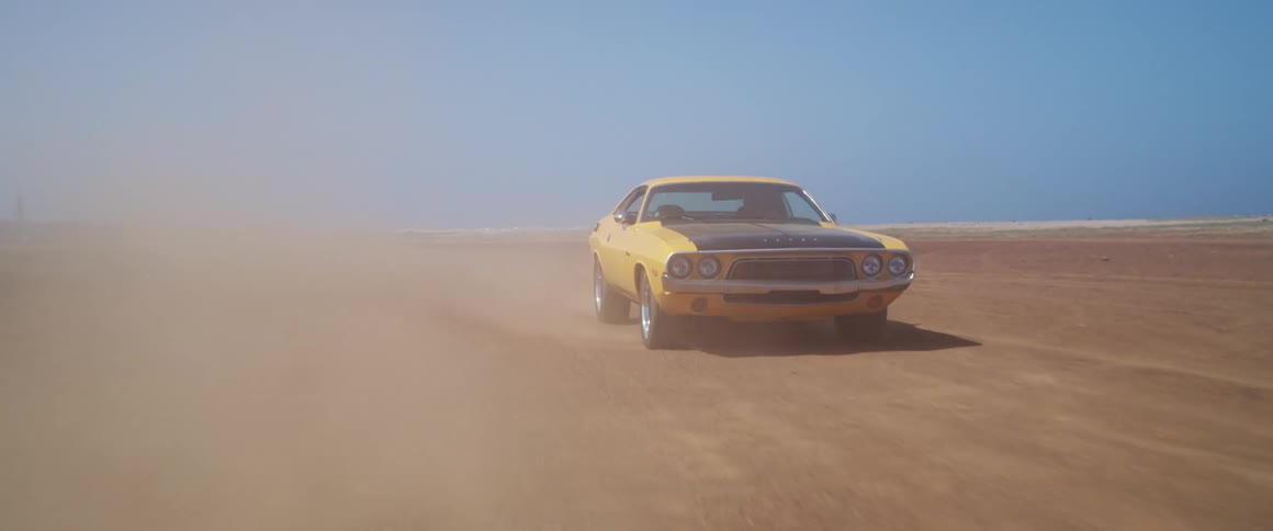 Yellow camaro driving on the desert kicking dust clouds