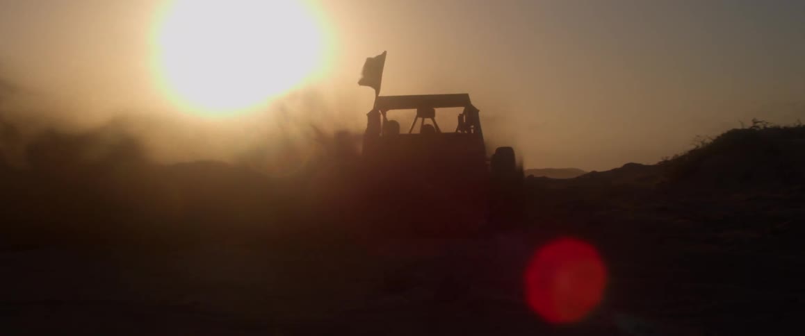 A man drives a dune buggy with a large through through a desert at dusk