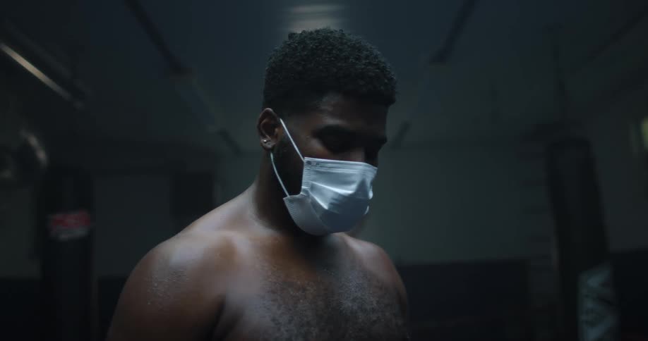 Man wearing a face mask standing and looking down inside of a boxing ring indoors