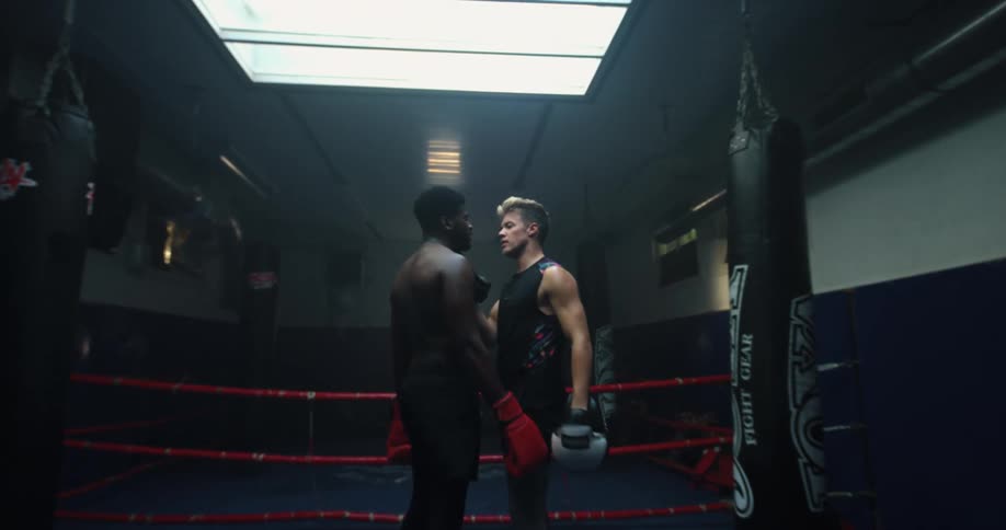 Two men in a boxing ring where one reaches over and kisses the other