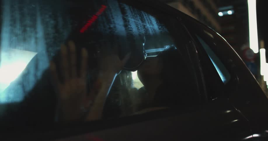 Two people kissing each other in a parked car at night time