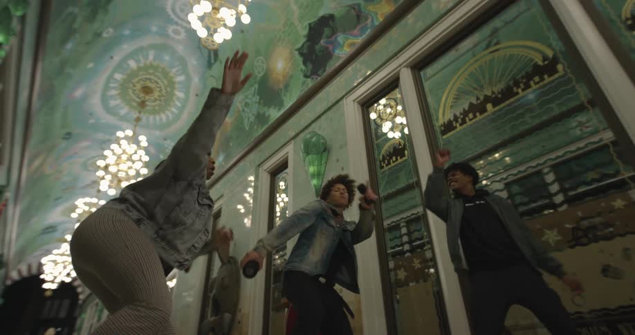 Teenagers dancing in a hallway with chandeliers hanging from the ceiling