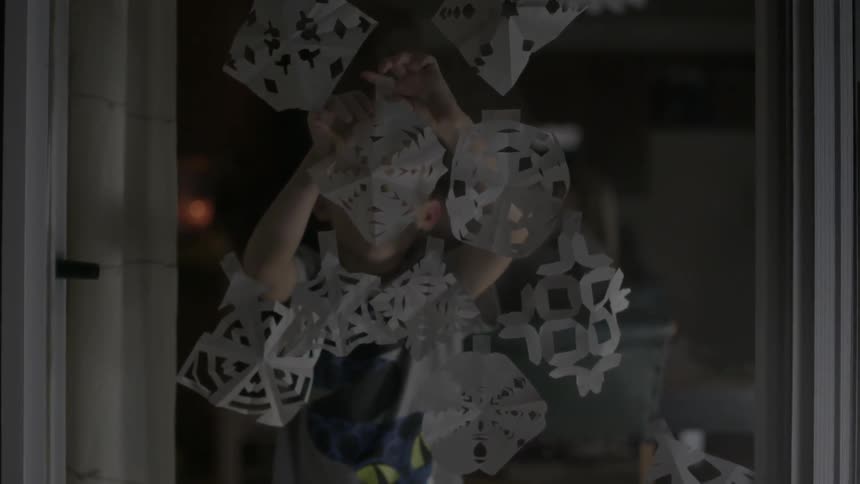 A child taping paper snowflakes to a window