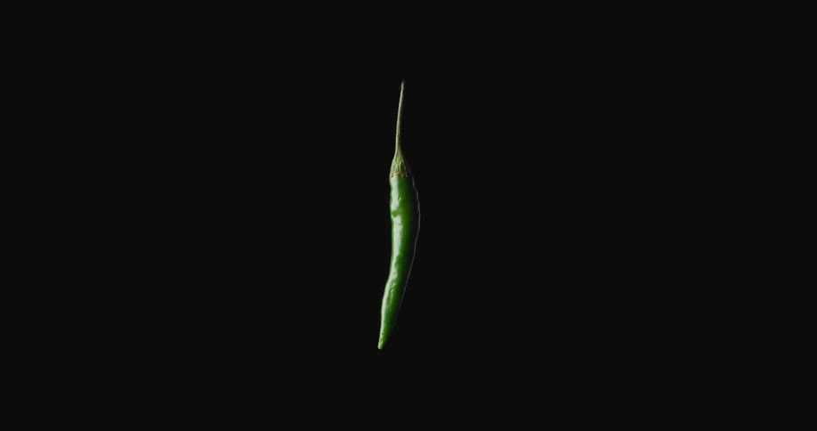 A green jalapeno suspended in mid air twirling around in circles