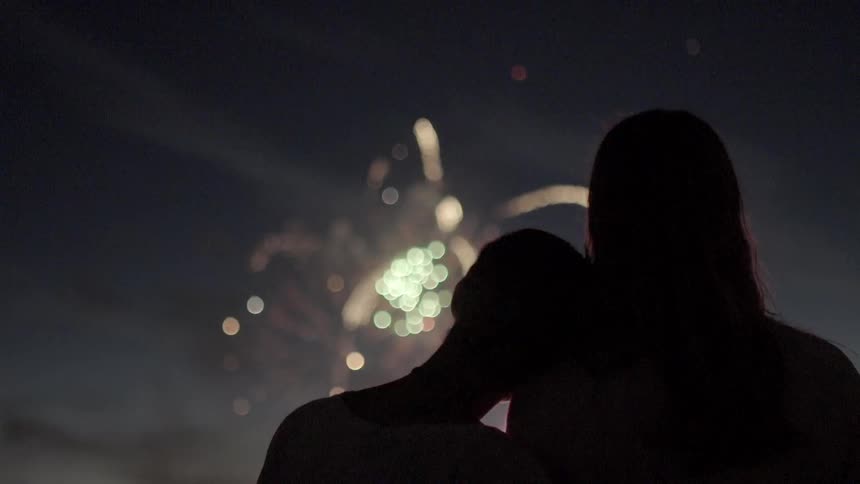 Two people watch a night sky as fireworks go off