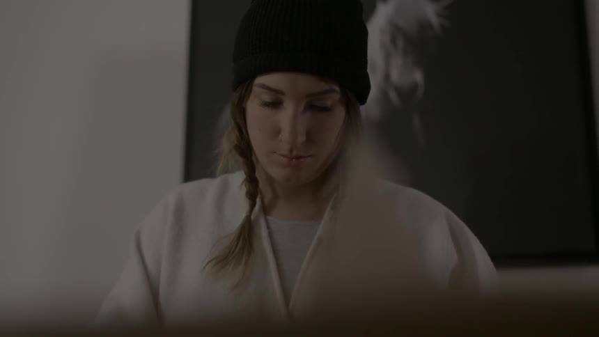 A woman is looking down with a painting behind her