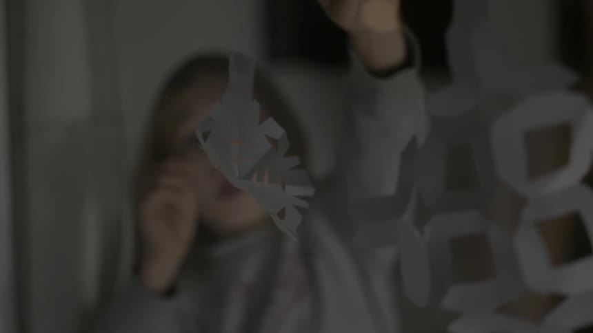 A young female child tapes a paper snowflake to a window