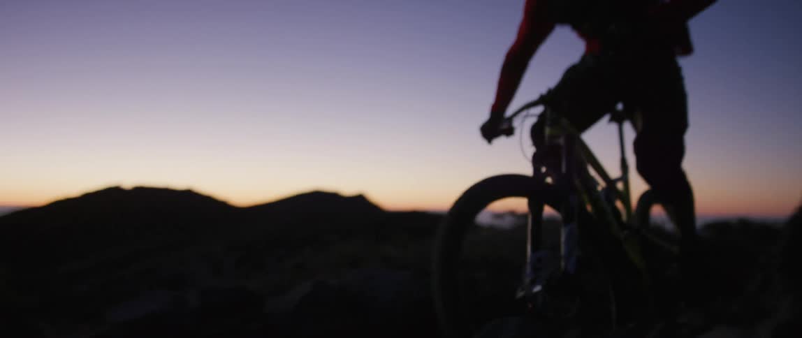 A silhouetted person riding a mountain bike in nature at dusk