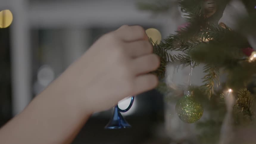 Person placing an ornament on a christmas tree