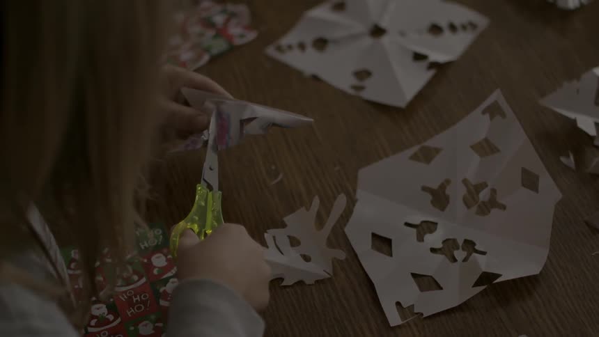 A young girl makes snowflakes with paper and scissors