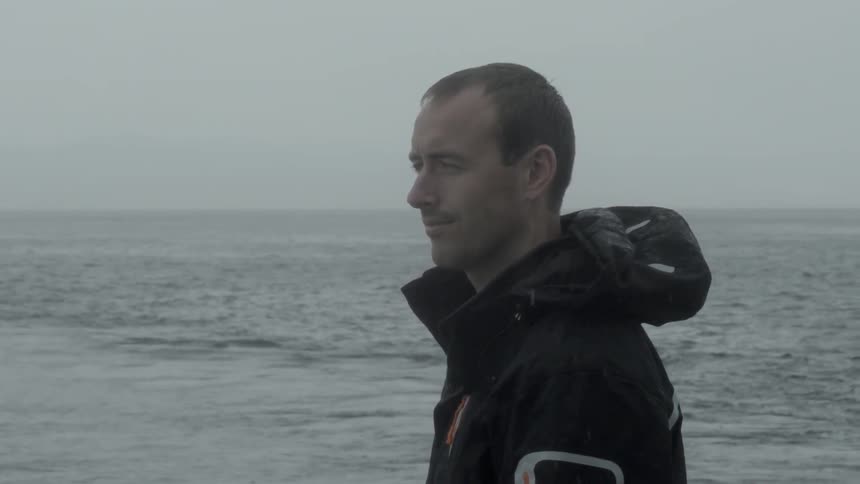 Man looking off in the distance near the ocean on a rainy day