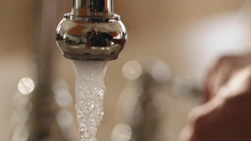 A person using their hand to turn on a faucet