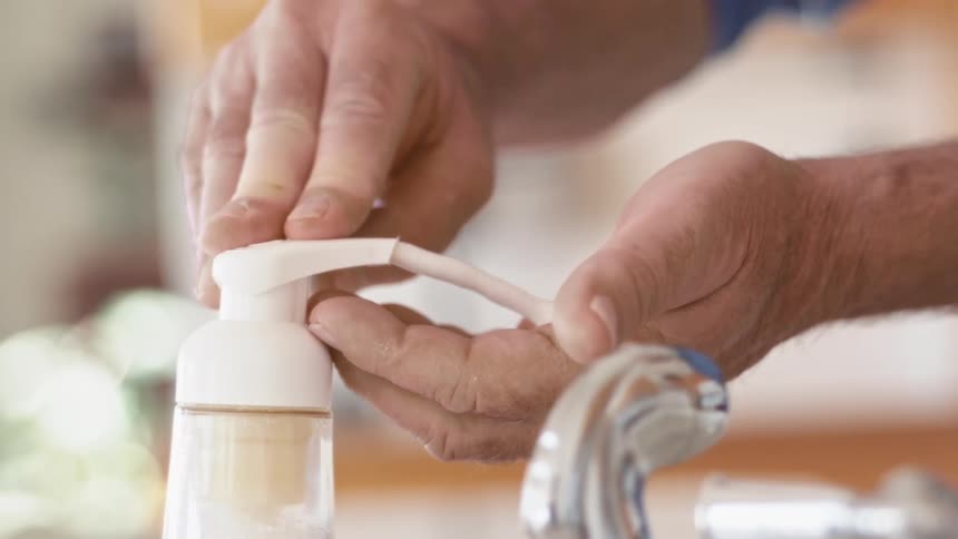 A hand pressing down a soap dispenser over the sink in the bathroom
