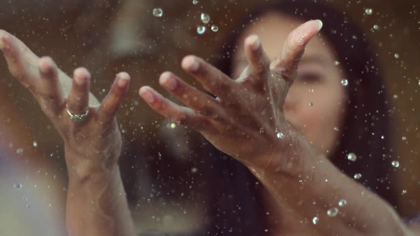 A woman holds her hands out as water rains down on them