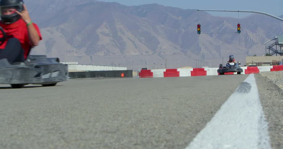 People are riding go carts around a track with mountains in the background