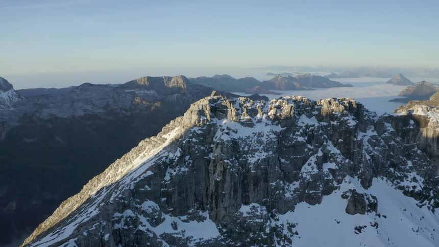 A cabin on a cliff with snow and ice with a mountain range the sky and clouds in the background
