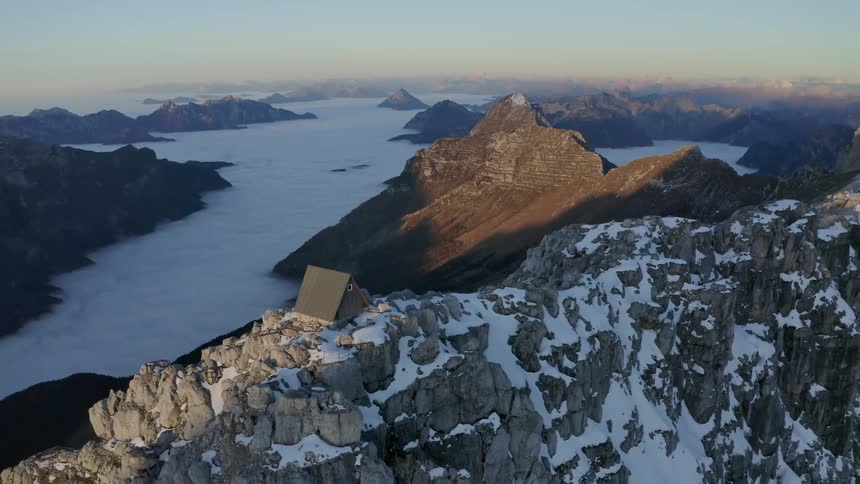 A lone building on the summit of a snowy mountain ridge in the evening