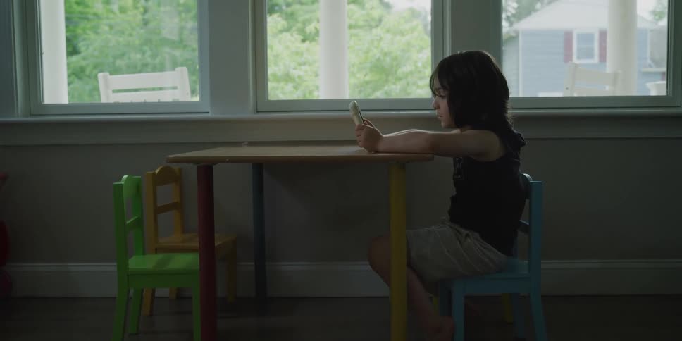 A young girl sits at a small table while holding a tablet computer in her hands