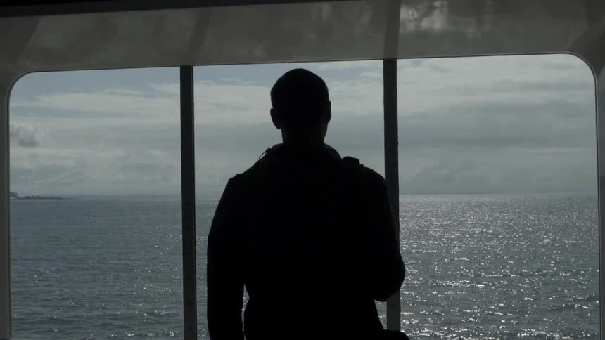 Silhouette of a man looking out of the window at the ocean