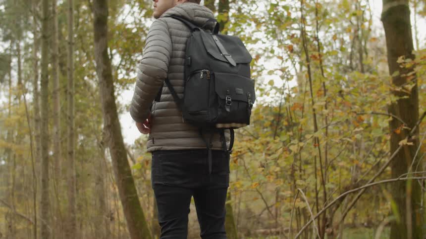 Man wearing a backpack looks at the sky while standing in a forest