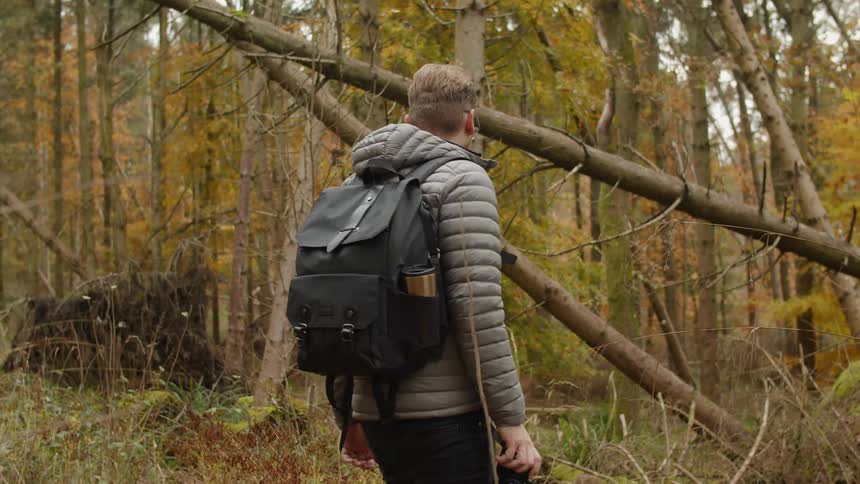 A man walks through a heavily wooded area with a backpack and binoculars