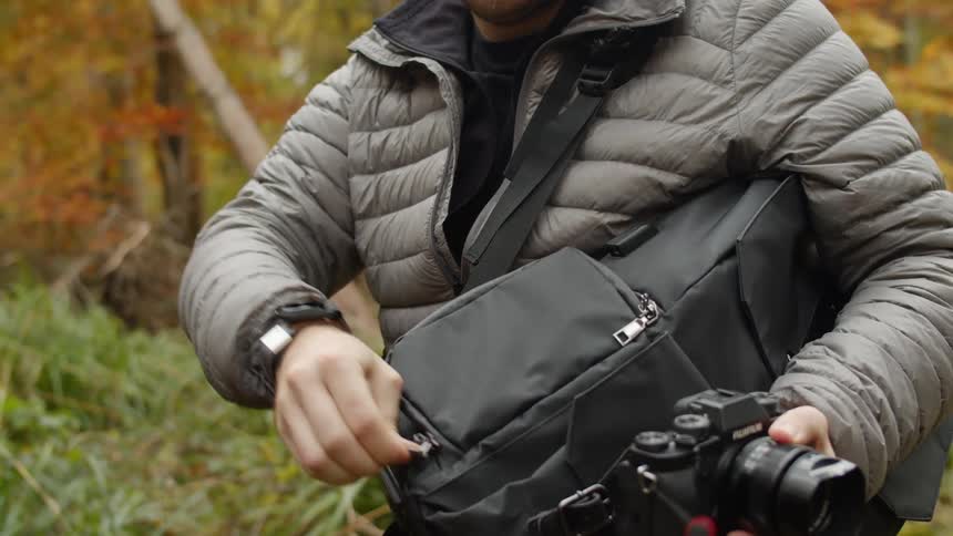 Man opening a black backpack putting a photography camera inside