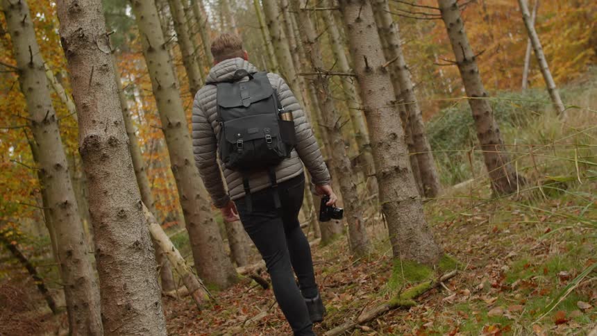 Man walking through an autumn forest holding a photography camera