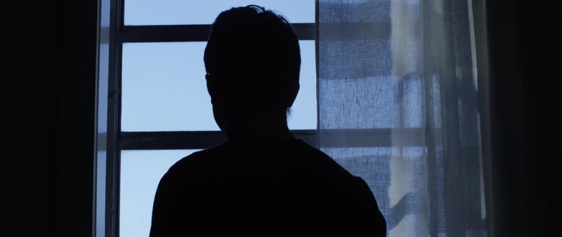 Man with glasses looking out the window is silhouetted against the sky
