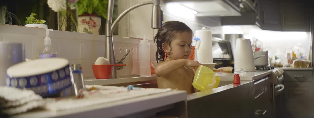 Little boy playing with toys while taking a bath in a kitchen sink