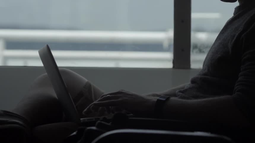 A man is typing on a laptop sitting near a window