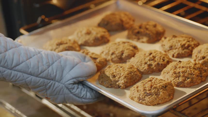 A person taking a tray of cookies out of an oven in a home kitchen