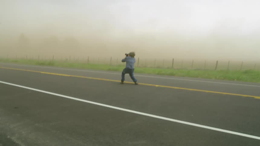 A man gets low to stay balanced as he photographs intense storm winds during a very strong severe thunderstorm