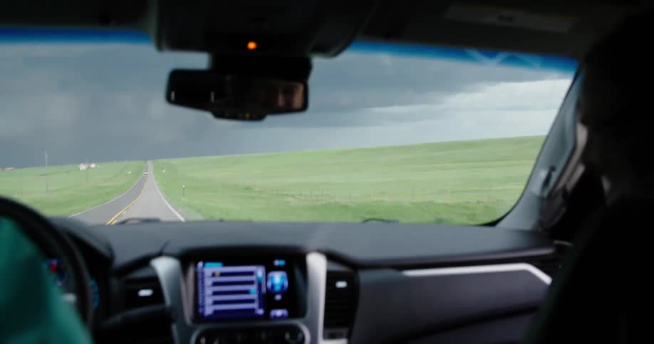 Wide hand held shot looking out the window of a fast moving vehicle as storm chasers drive straight towards a supercell severe weather thunderstorm
