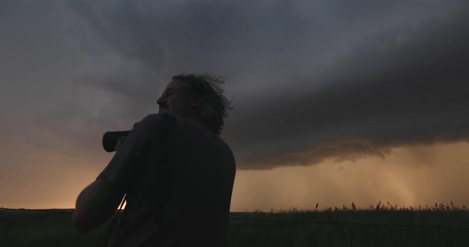 The calm before the storm as a man with a camera  photographs a massive thunderstorm illuminated by golden sunset light