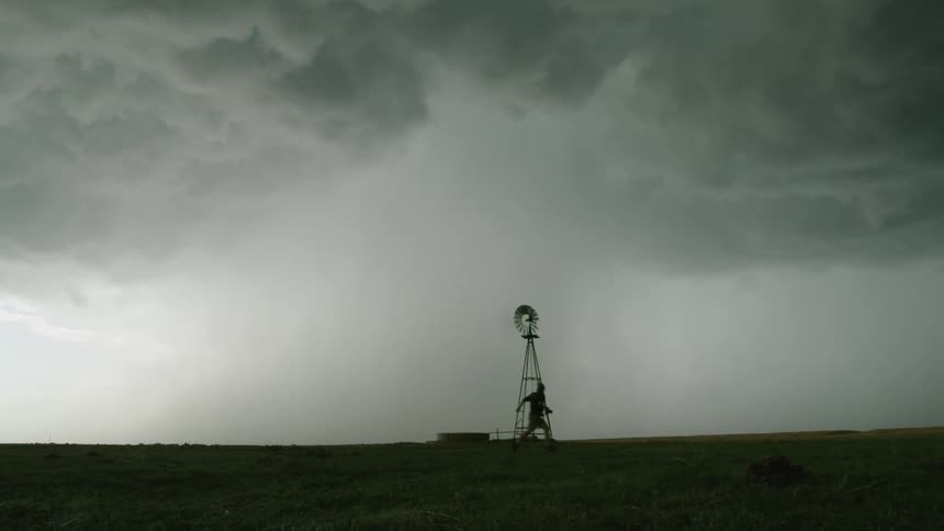 Silhouette of a man sprinting across a field with intensity and purpose with an old windmill and massive severe supercell thunderstorm behind him rapidly approaching