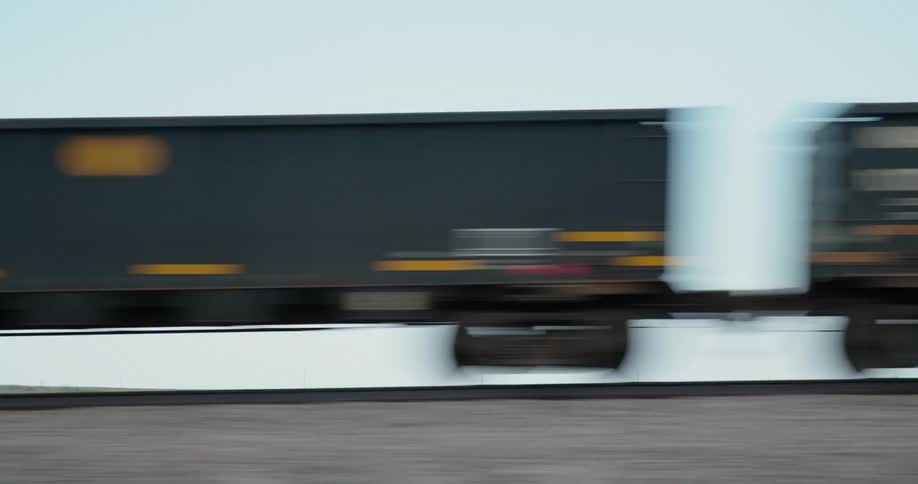 From. the point of view of the driver looking out the window at box rail cars in a freight train rapidly passing by on train tracks