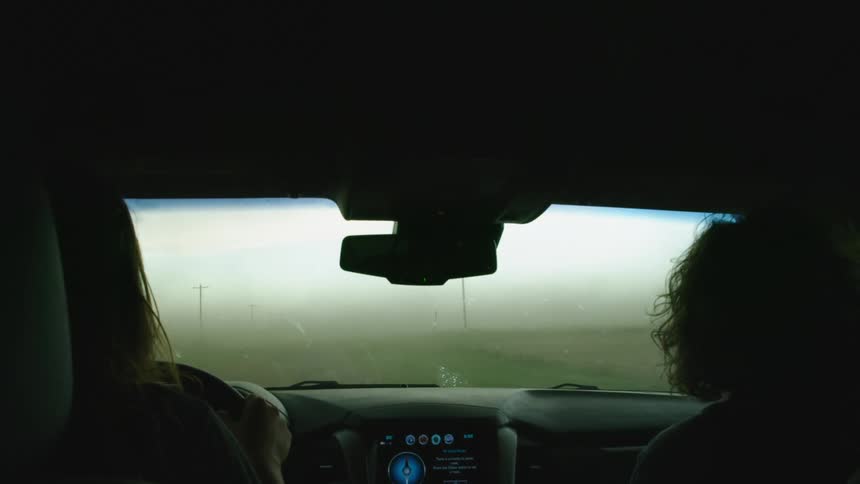 A woman and man drive through a severe dust storm in rural America as strong downdraft winds whip up sand, topsoil and other debris making treacherous driving conditions