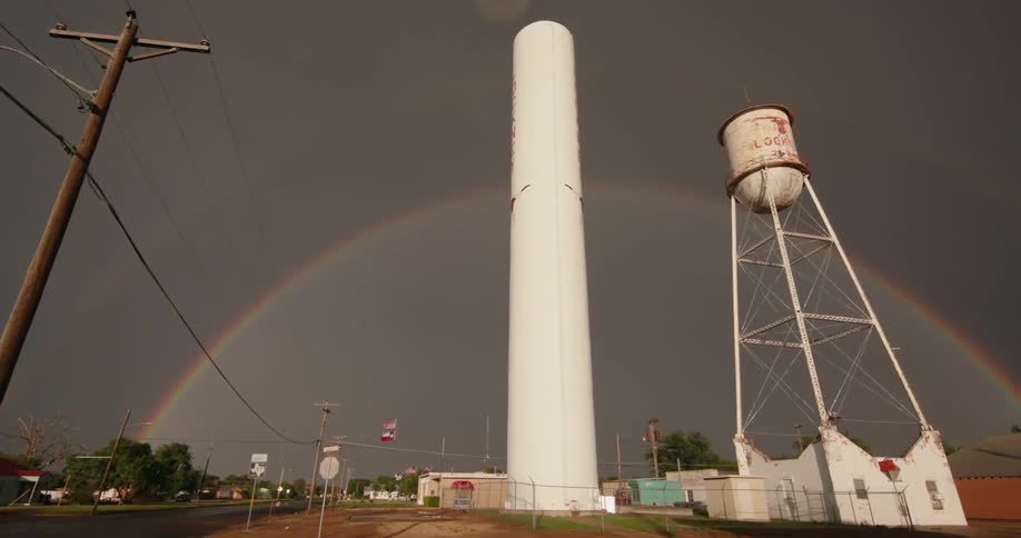 A massive rainbow spans an old water tower and smoke stack in a small town in rural Texas after a thunderstorm struck the area in spring