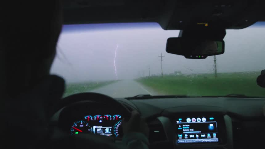 Slow motion shot of a woman driving stormchasers as a massive bolt of lightning strikes in the middle of the road in this dramatic shot
