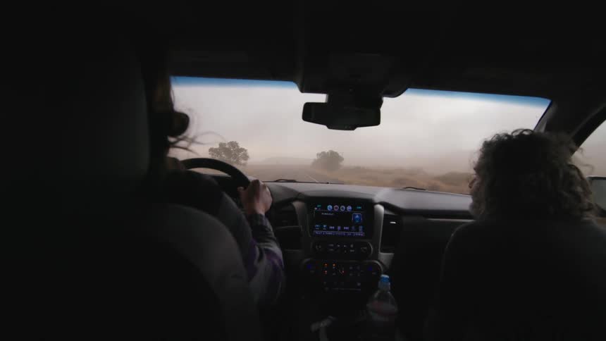 A male photographer and female stormchaser drive through extreme winds chasing a tornado supercell storm
